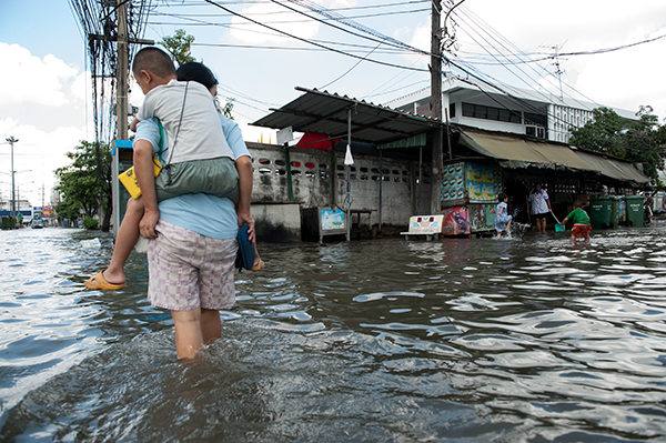 man walking in flooded street carrying child