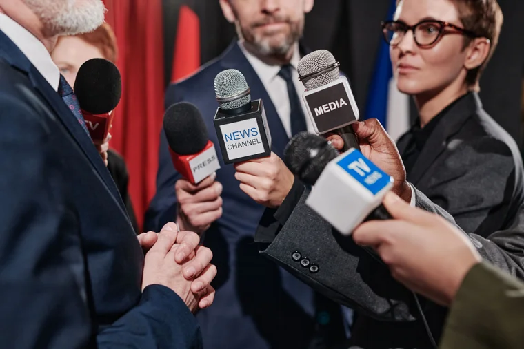 group of reporters holding microphones up to a speaker